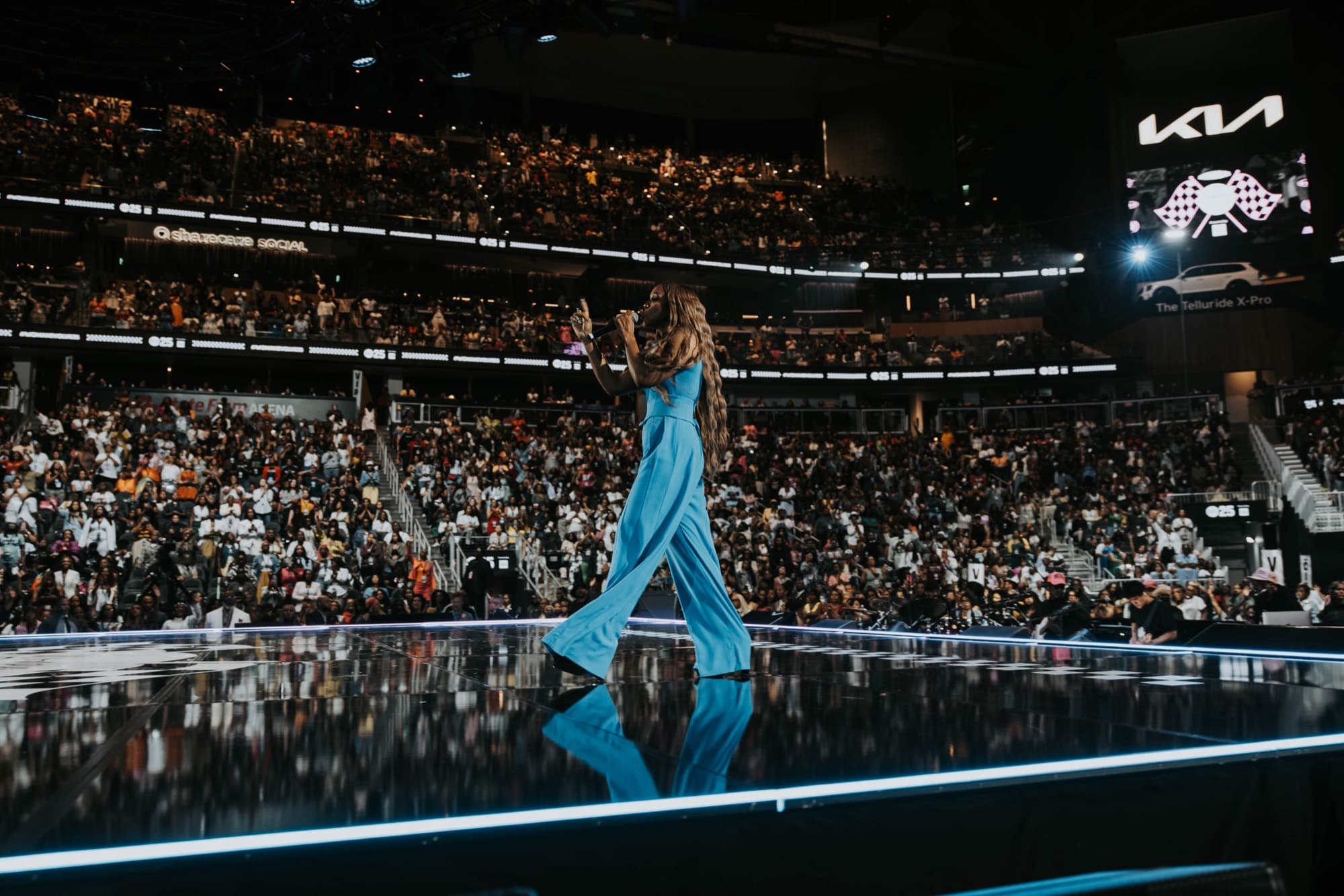 A performer crosses an arena stage in front of a packed crowd during Woman Evolve 2025